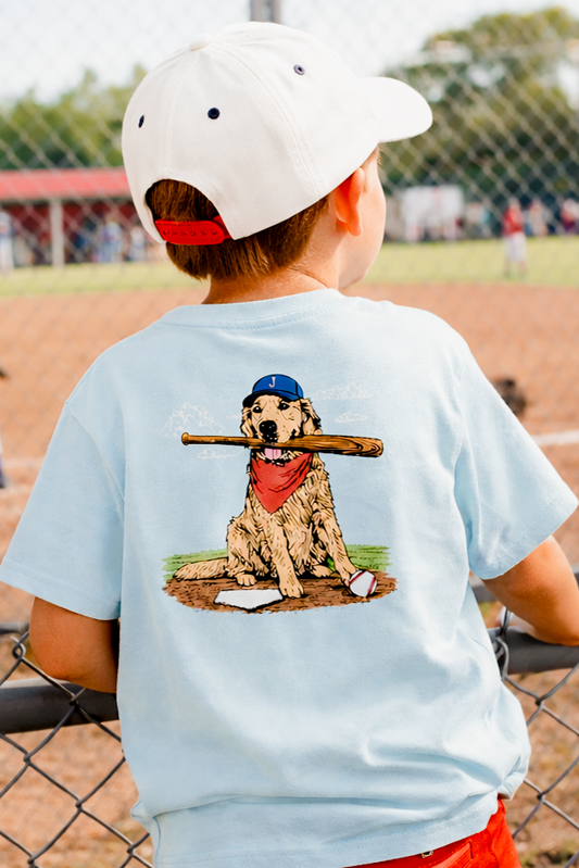 Child wearing a light blue t-shirt with a dog graphic on a baseball field.